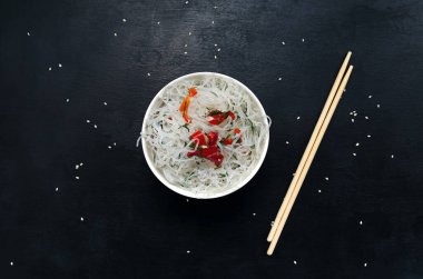 Asya yapımı cam fungoza pirinç eriştesi ve bambu çubuklarını siyah bir arka plan üzerinde susam tohumlarıyla dolu beyaz yuvarlak bir kasede fotokopi alanı ile kapatın. Veganlık, yağsız yiyecekler, esneklik