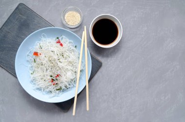 Asya mutfağı. Bambu çubukları, soya sosu ve susam tohumlarıyla mavi bir tabakta sebzeli, biberli ve otlu Fungose cam pirinç eriştesi.