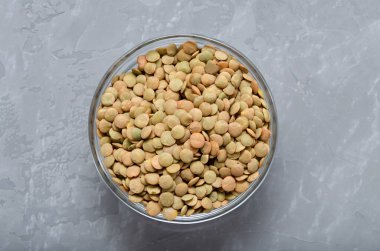 Camdan bir kasede mercimekler. Gri arka planda, fotokopi alanı olan bir yere saçılmış. Sağlıklı beslenme düzeni. Veganlık. yağsız yiyecekler.