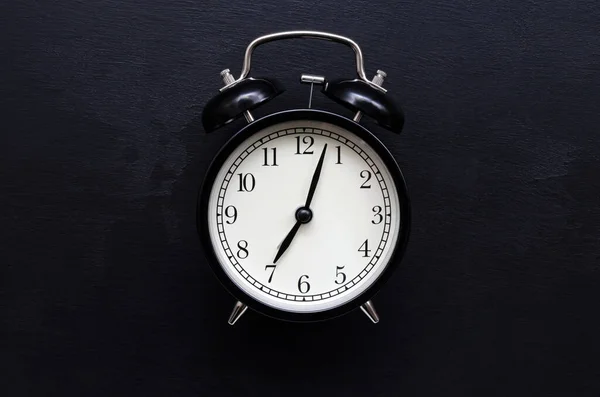A black alarm clock with a white dial shows the time of 7 hours on a black slate background with place for text — Stock Photo, Image