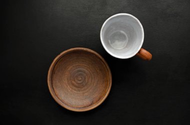 Boş kahverengi seramik sofra takımı kupası ve siyah bir arka planda tabak. Yemek konsepti ve onun yokluğu..