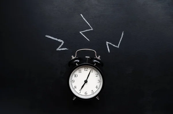 Un reloj despertador negro con esfera blanca muestra el tiempo de 7 horas y anillos en un fondo de pizarra negro con lugar para el texto —  Fotos de Stock