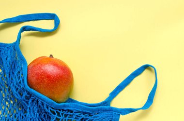 Sarı arka planda sicim torbasında, yazı için yeri olan parlak, egzotik, sulu bir mango meyvesi. sıfır atık konsepti. çevre dostu yeniden kullanılabilir materyaller