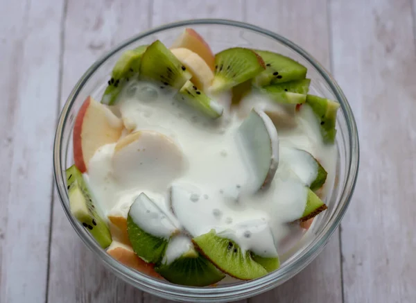 Fresh fruits salad with cream in bowl on wooden background Royalty Free Stock Images