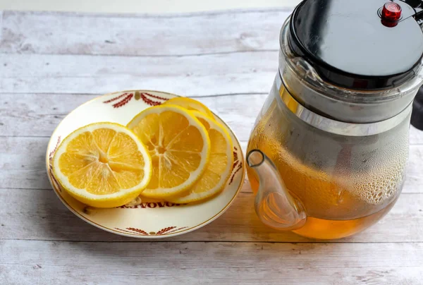 Tetera, limón. Tetera de vidrio con té verde, la mitad de limón sobre fondo de madera . —  Fotos de Stock