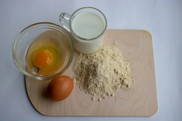 Baking cake in rustic kitchen - dough recipe ingredients eggs, flour, milk, on white planked wooden table from above. Background layout with free text space.