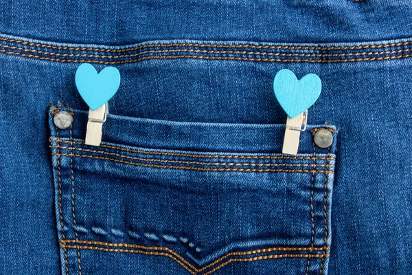Small wooden heart clothespins fastened to a denim pocket. Small clothespins with blue hearts on the pocket of blue jeans. — Stock Photo, Image