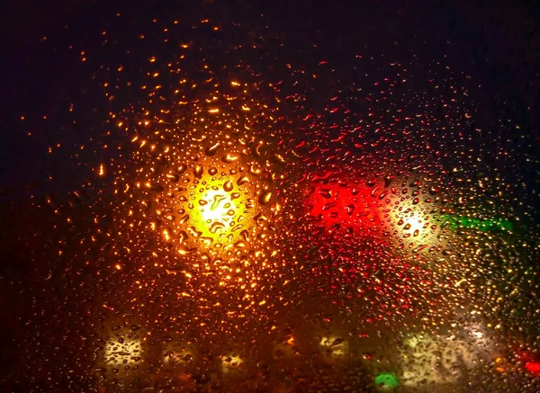 Gocce di pioggia sul finestrino con luce stradale bokeh, goccia d'acqua sul vetro, tempesta notturna pioggia concetto di guida auto. auto notturna — Foto Stock