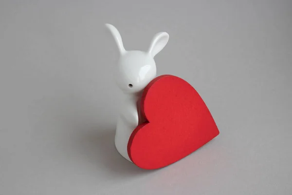 Hermoso conejo de cerámica sobre fondo blanco. estatuilla de un conejo blanco con un corazón rojo.Decoración de Pascua — Foto de Stock