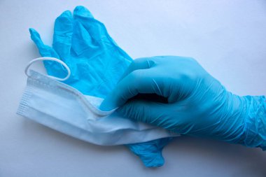 Mavi lateks eldivenli bir adam beyaz arka planda bir maske tutuyor. Ellerini ve yüzünü virüslerden koru.