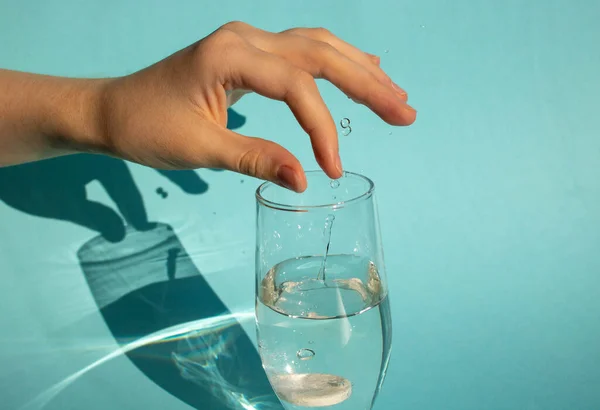 На голубом фоне рука сбрасывает растворяющуюся таблетку аспирина в стакан воды — стоковое фото