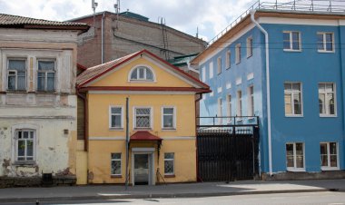 İki katlı küçük sarı bir ev. Büyük evlerin arasına sıkıştırılmış..