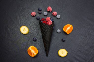 Taze yabanmersini, ahududu, siyah arka planda siyah waffle külahlı portakal.