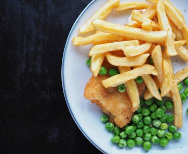 Koyu grunge arka planında yeşil bezelyeli balık ve patates kızartması.