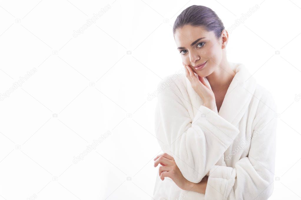 Beautiful and natural woman in white bathrobe is touching her skin. Relax and comfortable feelings only.