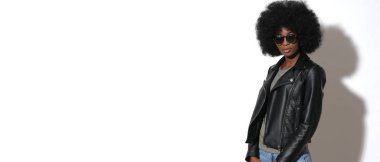 Siyah derili seksi afro kız, kayalık ceketli ve beyaz arka planda siyah güneş gözlüklü..