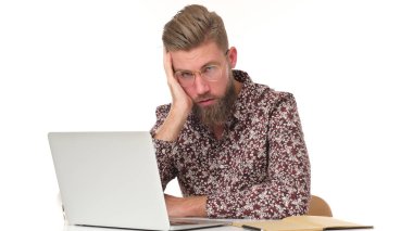 Sıkıcı sakallı genç işçi bilgisayarın önünde oturuyor..