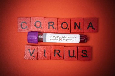 Kırmızı arka planda scrabble harfleriyle çevrili pozitif Coronavirus testi yapılmış kan örneği..