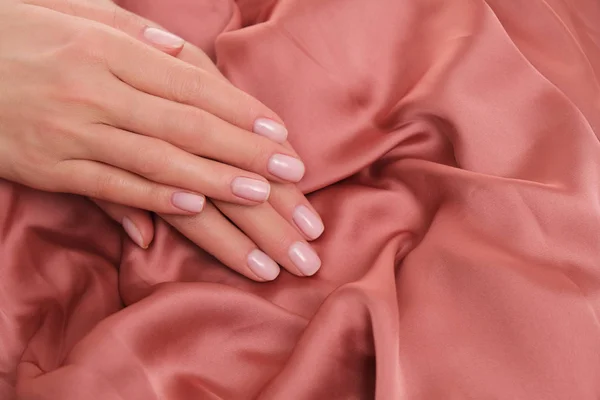 美丽的女性手 有着精致 自然的修指甲 躺在缎子上 漂亮的浅粉色泽 — 图库照片