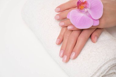 Kadın ellerinde güzel, narin bir manikür. Mor orkideyle beyaz havlunun üzerinde uzanmış eller resmi..