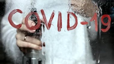 Camdaki kırmızı boyalı COVID-19 yazıları suyla yıkanmış. Sprey şişeli bir el, virüssüz.