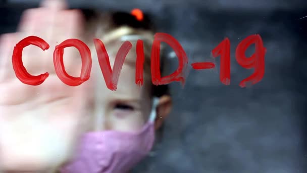 Блондинка покриває руку червоними літерами COVID-19 на склі, дівчина в медичній масці, сидить вдома, ізоляція, напис червоною фарбою, карантин — стокове відео