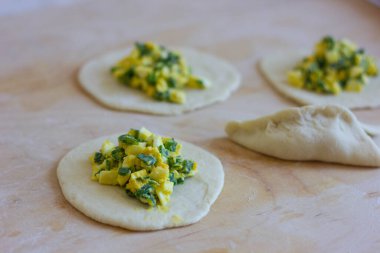 Yeşil soğan ve yumurtalarla doldurulmuş yuvarlak bir hamur parçası. Soğanlı turtalar ve yumurtalar. Rus mutfağı. Yemek pişirme. Sarı-yeşil dolgu. bitmiş hamur.