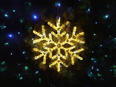 Sarı parlak bir kartopu şeklinde dekorasyon. Noel ağacında iğne ve mavi ışıklardan oluşan bir arka planda.