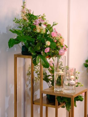 Ahşap raflarda duran gül buketleri, vazolarla birlikte, içinde bir mum bulunan ahşap bir alayı yakıyor.