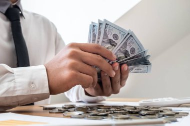 Önünde dolar ve sikke tutan işadamları, tasarruf etmek, başarılı işletmeleri genişletmek ve emeklilik için tasarruf etmek için grafikler hesaplıyorlar.