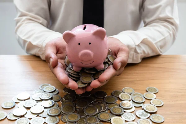 The hand of a businessman who holds a coin with a piggy bank to save money, grow a successful business, and save for retirement concept