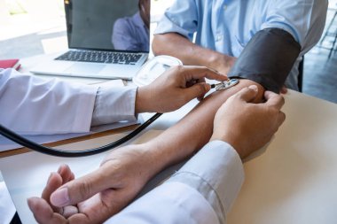 Erkek doktor kan basıncını ölçtü, hasta kalp atışlarını inceledi ve sağlık hizmetlerinden yakından bahsetti.
