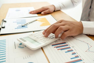 Bir iş adamı masada oturuyor ve gayrimenkul yatırımlarının finansal grafiklerini hesaplıyor.