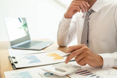 Bir iş adamı masada oturuyor ve gayrimenkul yatırımlarının finansal grafiklerini hesaplıyor.