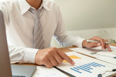 Bir iş adamı masada oturuyor ve gayrimenkul yatırımlarının finansal grafiklerini hesaplıyor.