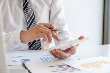 Bir iş adamı masada oturuyor ve gayrimenkul yatırımlarının finansal grafiklerini hesaplıyor..