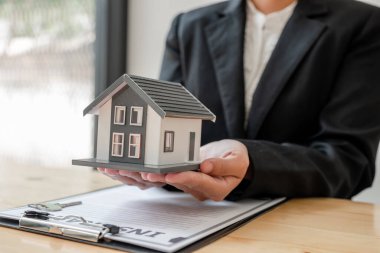 Bir ev sigortası acentesinin eli müşterilerin güvenliğini sağlamak için bir model ev tutmaktadır..