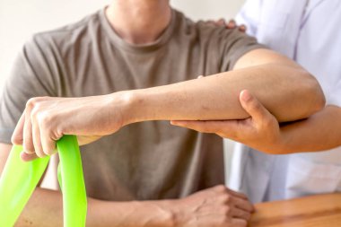 Kadın fizyoterapistler, dirsek yaralanması olan erkek hastalara rehabilitasyon merkezlerindeki hastaları muayene etmede yardımcı oluyorlar. Fizyoterapi kavramları.