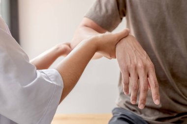 Kadın fizyoterapistler, dirsek yaralanması olan erkek hastalara rehabilitasyon merkezlerindeki hastaları muayene etmede yardımcı oluyorlar. Fizyoterapi kavramları.