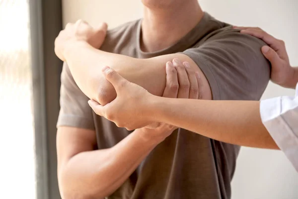 Kadın fizyoterapistler, dirsek yaralanması olan erkek hastalara rehabilitasyon merkezlerindeki hastaları muayene etmede yardımcı oluyorlar. Fizyoterapi kavramları.