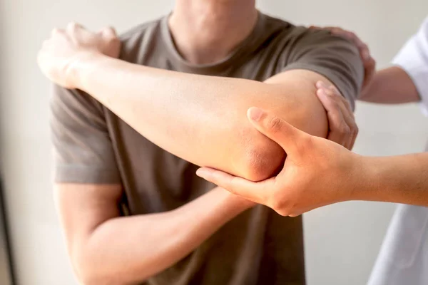 Kadın fizyoterapistler, dirsek yaralanması olan erkek hastalara rehabilitasyon merkezlerindeki hastaları muayene etmede yardımcı oluyorlar. Fizyoterapi kavramları.