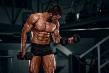 Spor salonunda kaslı adamlar ağırlık kaldırıyor.