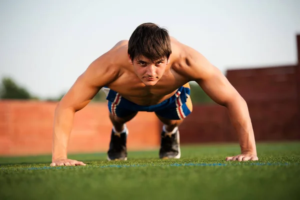 Outdoor sport, fitness training. Handsome Young Men Doing Pushups Outdoors in the Sport Field on a Sunny day
