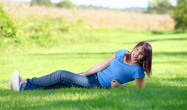 Beautiful young woman in jeans lying on the grass — Stock Photo, Image