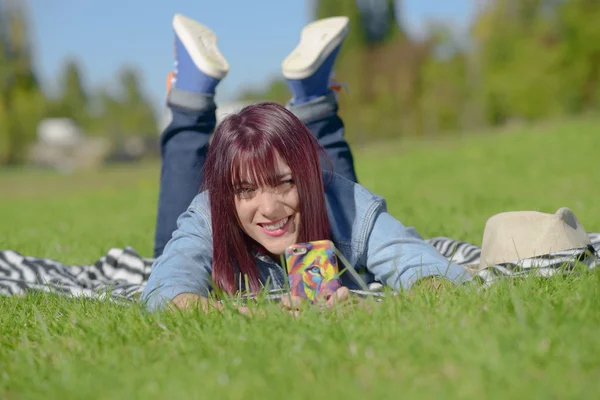 Mooie jonge vrouw in spijkerbroek liggend op het gras — Stockfoto