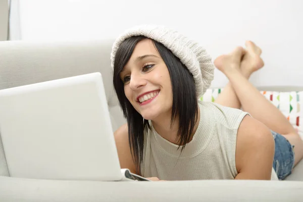 Jonge brunette student liggend op de Bank met een laptop — Stockfoto