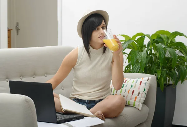 Joven estudiante bebiendo jugo de naranja en el sofá — Foto de Stock