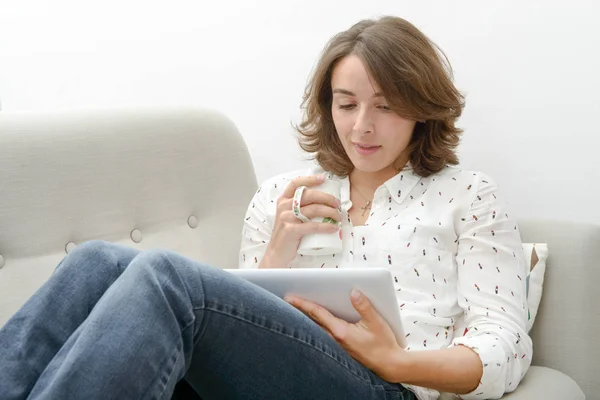 Mujer joven con una tableta bebe una taza de té — Foto de Stock