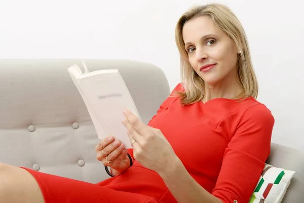 Beautiful blonde woman reads a book in the sofa
