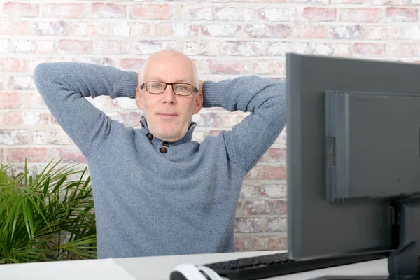 Ώριμος άνδρας με τον υπολογιστή είναι ξεκούραστη στο γραφείο του — Φωτογραφία Αρχείου